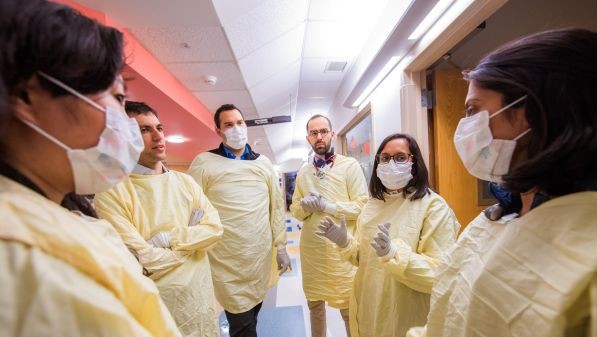 Students and faculty round together, donning medical gowns and face masks.