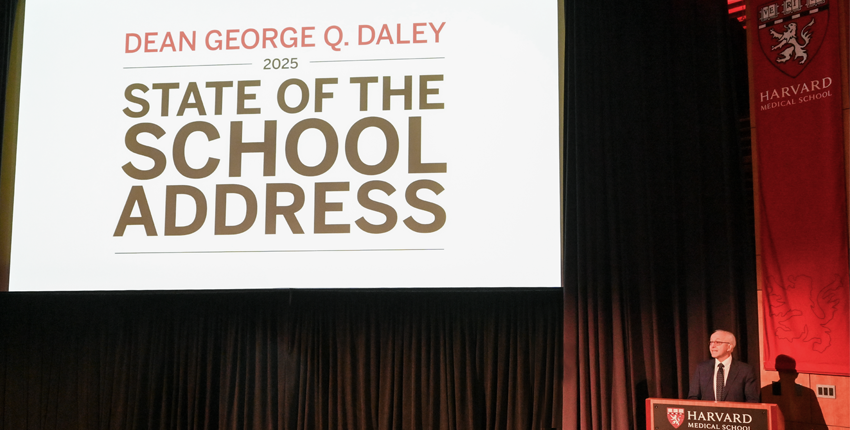 A large white screen that says "Dean George Q. Daley 2025 State of the School Address," next to Dean Daley standing at a lectern