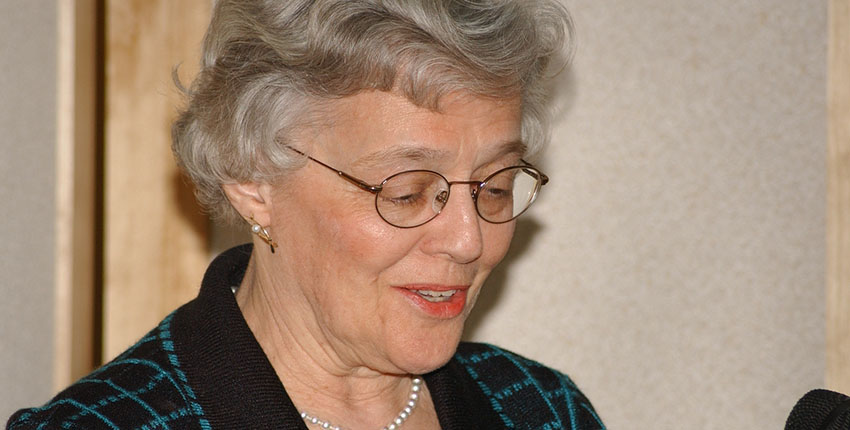 A smiling woman looks down at something off-screen.