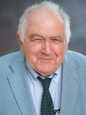 A close-up of a man in a suit with a wry smile.