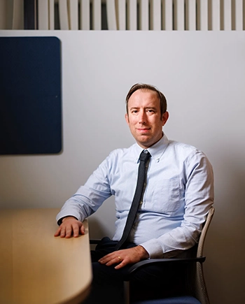 A man in a tie in an office smiles slightly at the camera