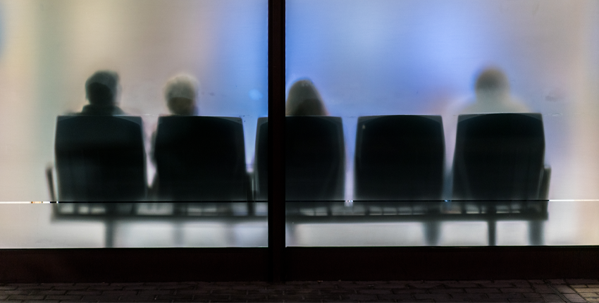 An abstract photograph of a waiting room with frosted glass and people sitting in chairs