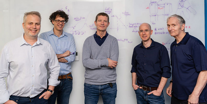 Group of five men standing at a whiteboard 