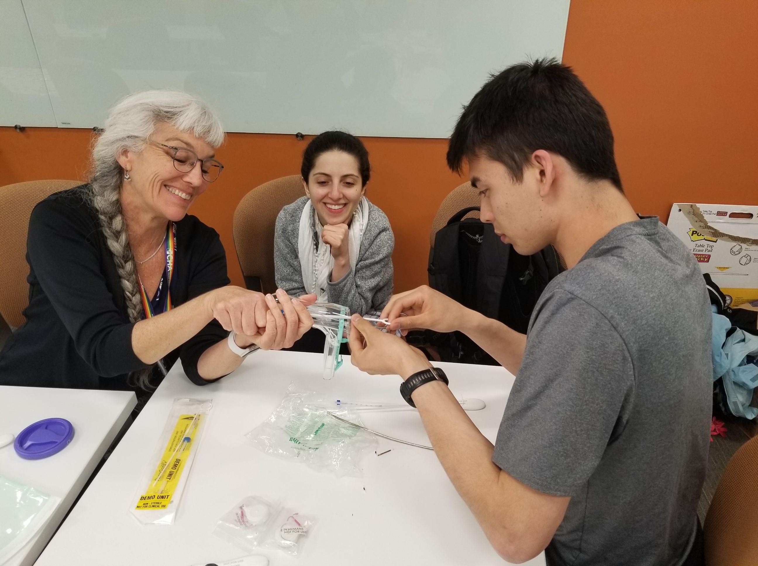 A professor is working with a student learning a clinical procedure while another student looks on.