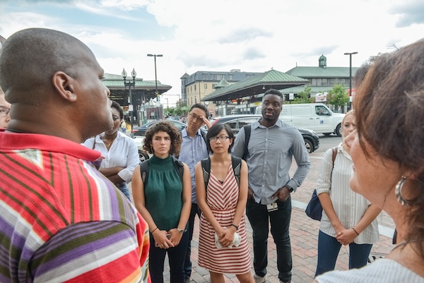 Students standing outside in Roxbury, MA, are listening to a community member.