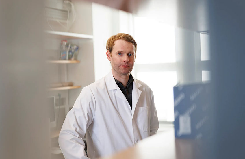 Photo of Andrew Kruse wearing a white coat in a bright lab space