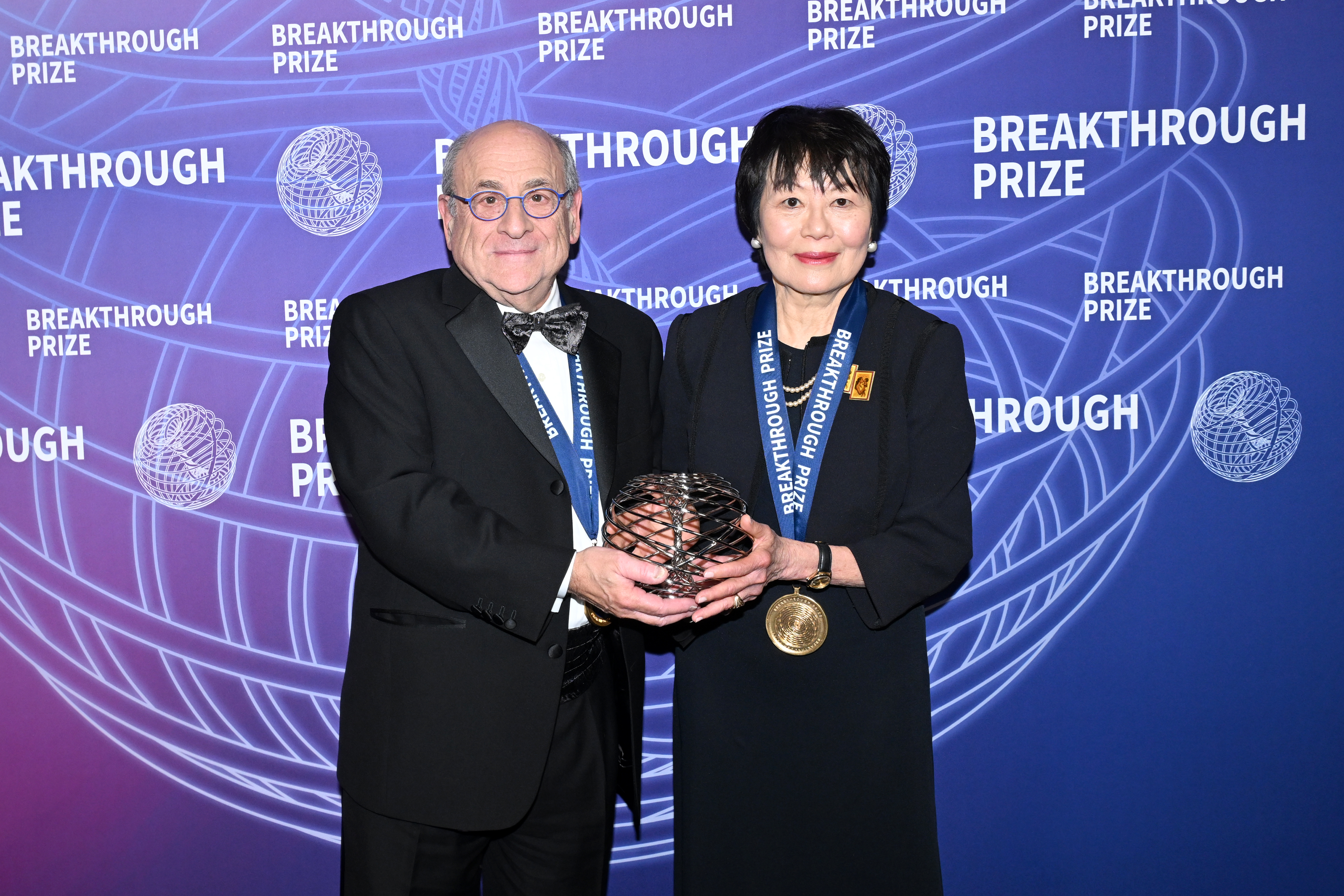 Stuart Orkin and Swee Lay Thein pose with their Breakthrough Prize. They wear medals around their necks.