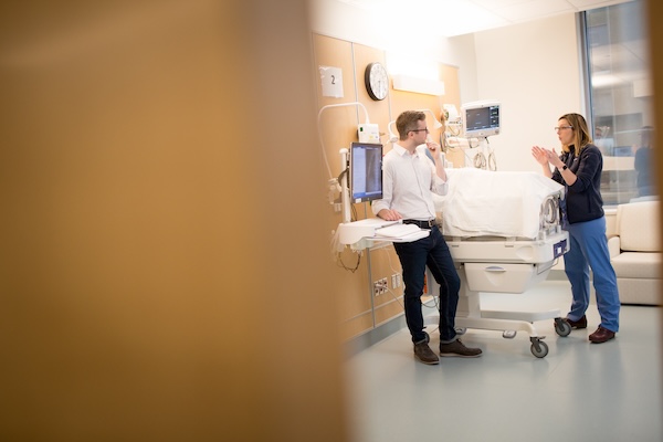 A medical student and teaching doctor converse while standing in a NICU bay over an incubator.