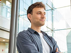 A man with blue shirt with glass windows in background