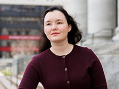 A woman in a burgundy button down sweater with marble building in background