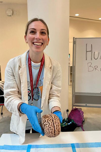 Kranz, wearing gloves and a lab coat and grinning, holds a preserved human brain over a table.