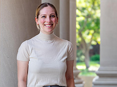A woman in a tan blouse stands in front of marble columns