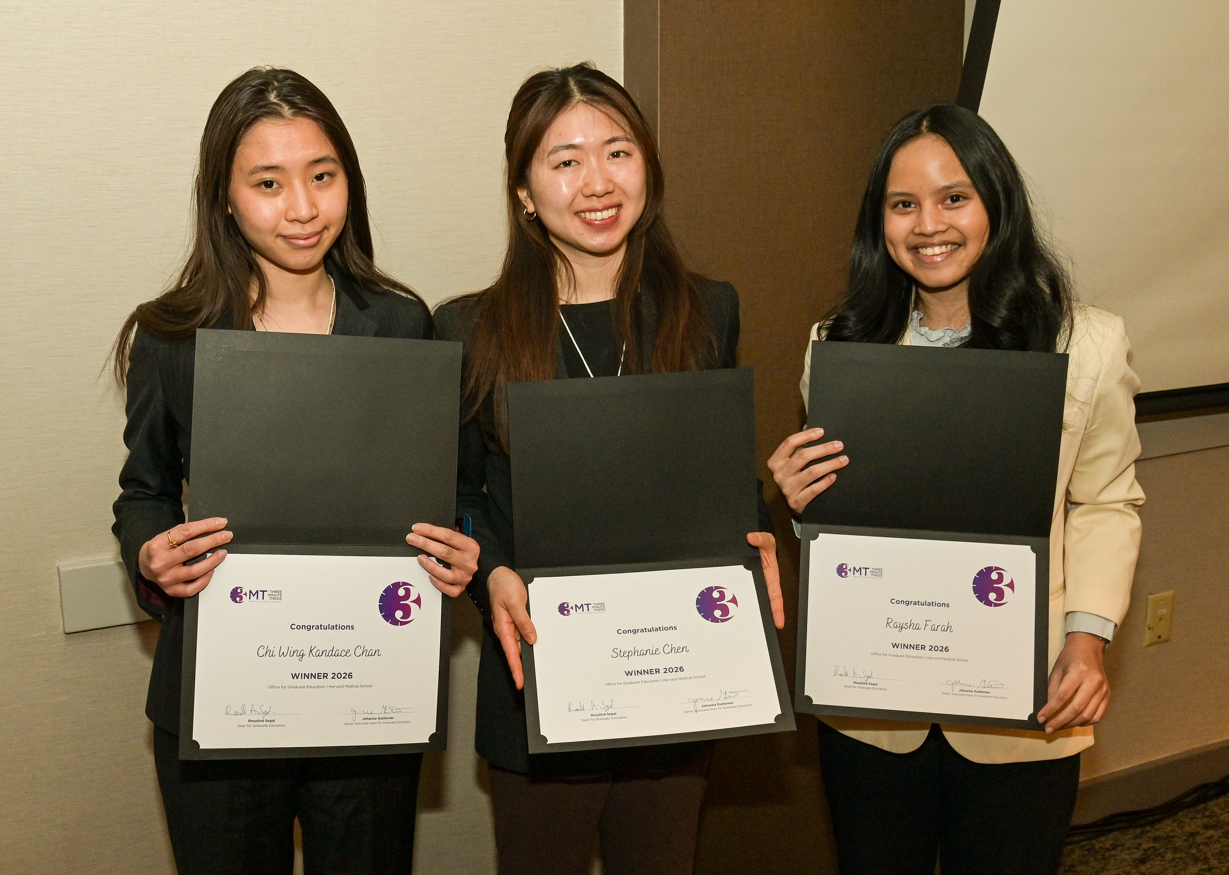 Three young women stand together smiling for the camera and holding certificates.