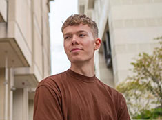 A man in a brown t-shirt with buildings in background