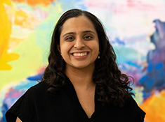 A woman smiling with a multicolored background behind her