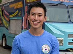 Man in a blue shirt in front of a van, both branded The Family Van