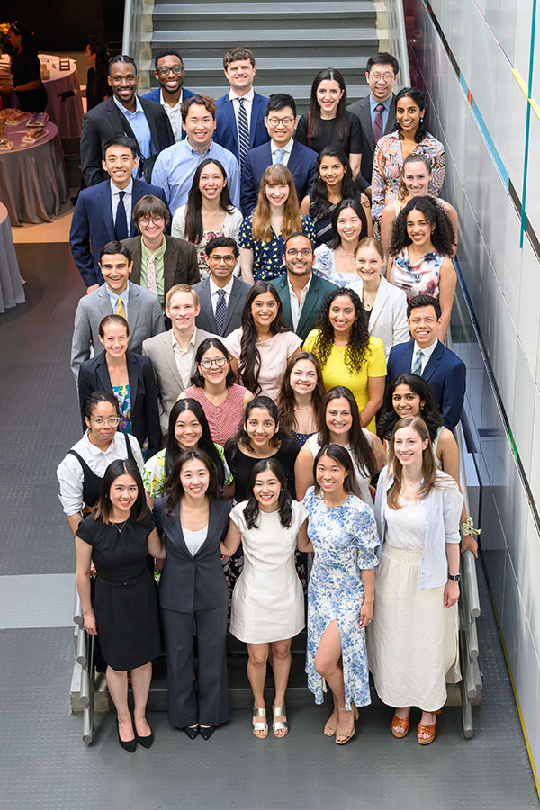 A group of about 35 young people stand staggered in rows on a set of stairs, smiling and looking at the camera.