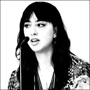 Black and white headshot photo of a young woman with long brown hair talking into a microphone