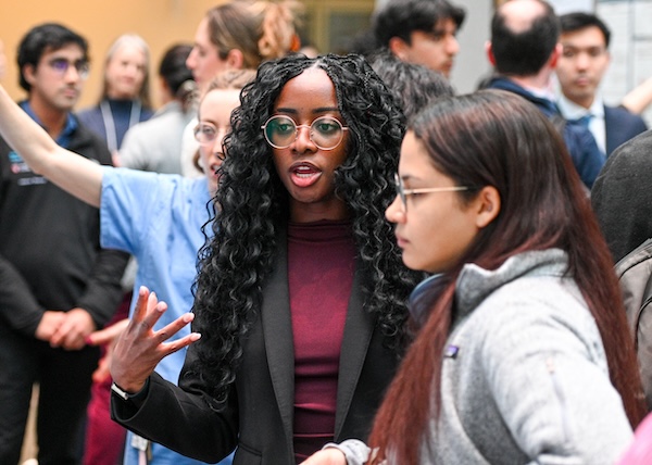 A med student is presenting her research to a fellow student while other students do the same thing in the background.