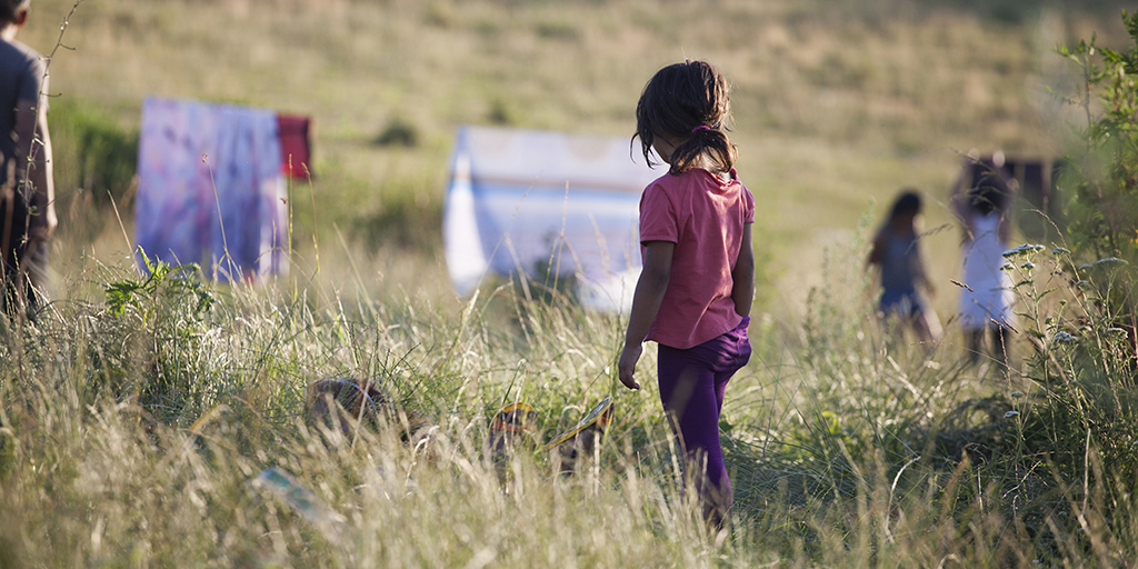the back of a little girl with a pink shirt walking in the grassy fields lonely. 