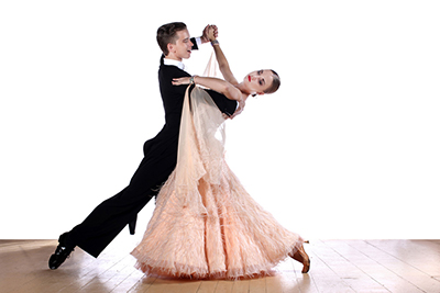 a man with a black tuxedo and a woman with a light pink dress hands interlocked and raised dancing.
