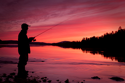 a silhouette of a man standing on a dock fishing under a bright red orange sky.