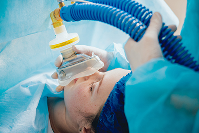 a woman laying down with a tub and face mask on getting her anesthesia treatment. 