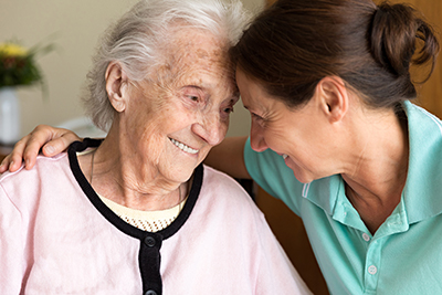 an elderly woman and a younger woman with their foreheads together smiling. 