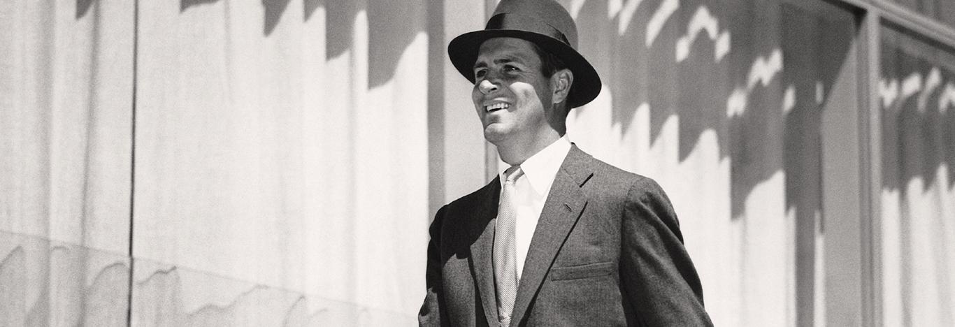 black and white photo of a smiling suited man wearing a fedora