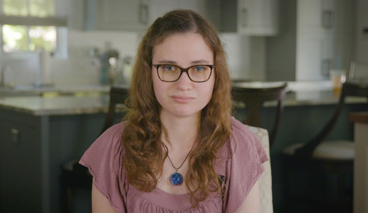 A shot of Jessica Chaikof from the chest up, wearing a pink shirt and glasses