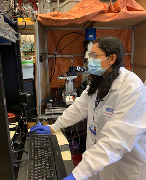 A student wearing gloves and a mask works on a desktop computer in the lab