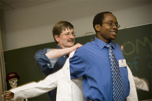 Above, Richard Mitchell, HMS associate professor of pathology and health sciences and technology and associate master of the HST society, helped Tafadzwa Muguwe into his white coat, a ritual that all new students take part in. 