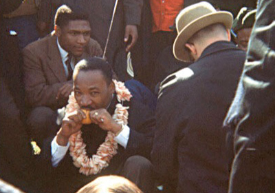 In Alvin Poussaint’s favorite personal photograph from the civil rights era, Martin Luther King Jr. eats an orange while taking a roadside break during the third Selma to Montgomery march in the spring of 1965. The lei around his neck was a gift to the march from the Hawaiian delegation. Photo by Alvin Poussaint.