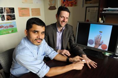Praveen Kumar Vemula of BWH and Jeffrey Karp, co-director of the Center for Regenerative Therapeutics at BWH, sit next to a graphic describing their team’s approach. Vemula holds a small jar representative of a cream containing the nanoparticles. He points to Karp’s finger as an example of where the cream could be applied; many people are exposed to nickel through jewelry like rings. Photo by Donna Coveney, Brigham and Women's Hospital.