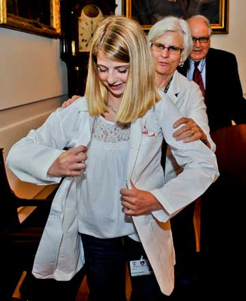 Gabby Samsock dons her white coat, assisted by Katherine Treadway, Gerald S. Foster Academy Associate Professor of Medicine. Behind them is Ron Arky, Daniel D. Federman, M.D. Professor of Medicine and Medical Education Master, Francis Weld Peabody Society. Photo by Steve Lipofsky. 