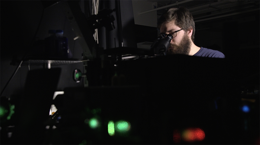 Man looking in a microscope, with lasers visible in foreground