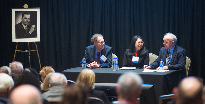 Three people sit at table in front of audience