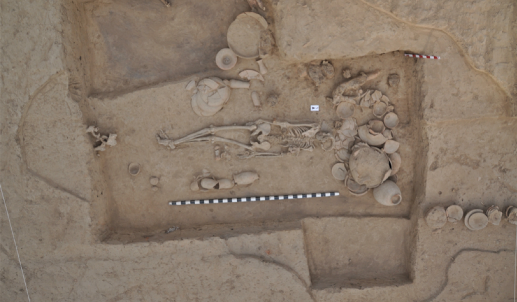 Photo of gravesite taken from above shows a skeleton and pots with a measuring stick