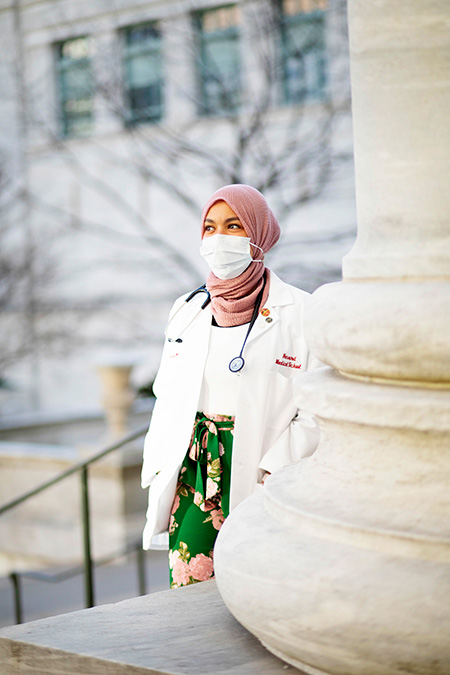 Photo portrait of Ahmed wearing a mask standing by pillar of Gordon Hall