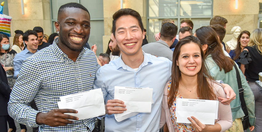 three students holding their match letters with a crowd behind them