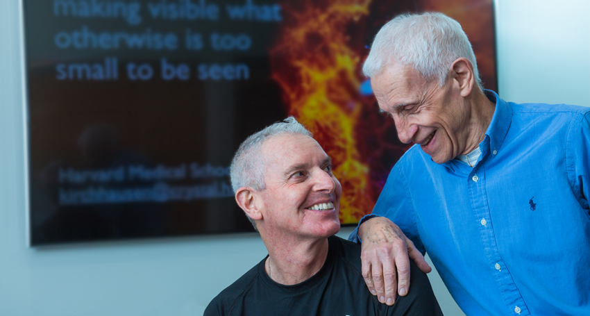 Harrison and Kirchhausen in front of a digital screen with molecular imagery looking into each other's eyes