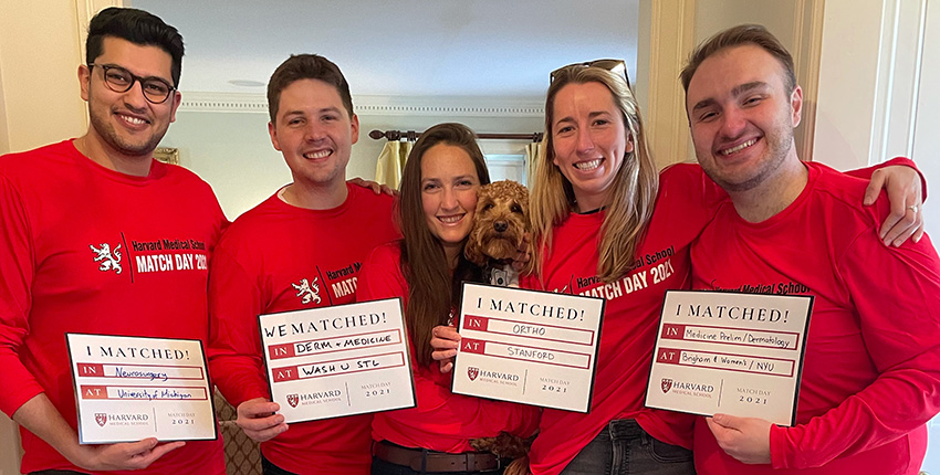 Three men and two women in red long sleeve T-shirts holding four signs that read I Matched and have written specialty and residency location hand written