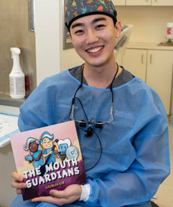 Jeremiah Kim in PPE holding The Mouth of Guardians book that has a colorful illustration on the cover