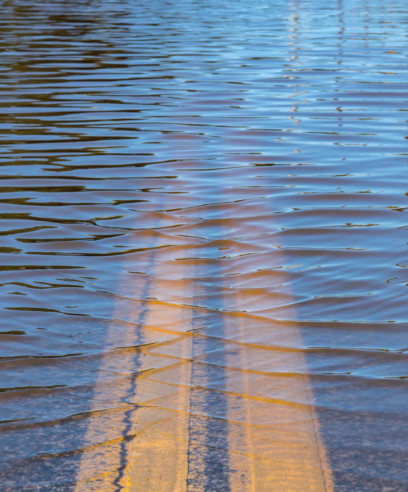 double yellow center lines of a road disappearing into deep water