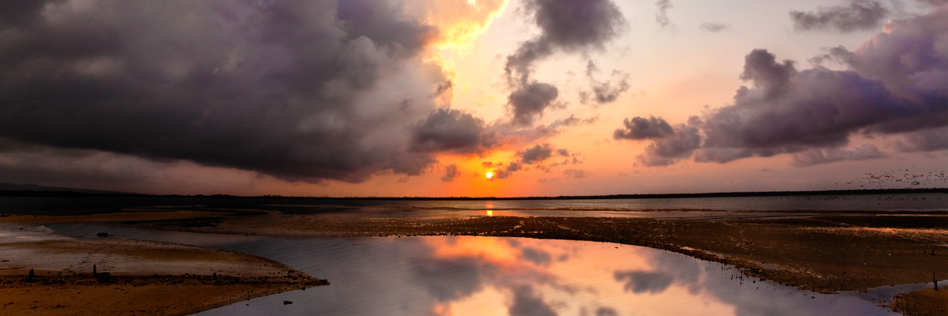 panoramic view of a orange and peach-colored sunset reflected in calm water