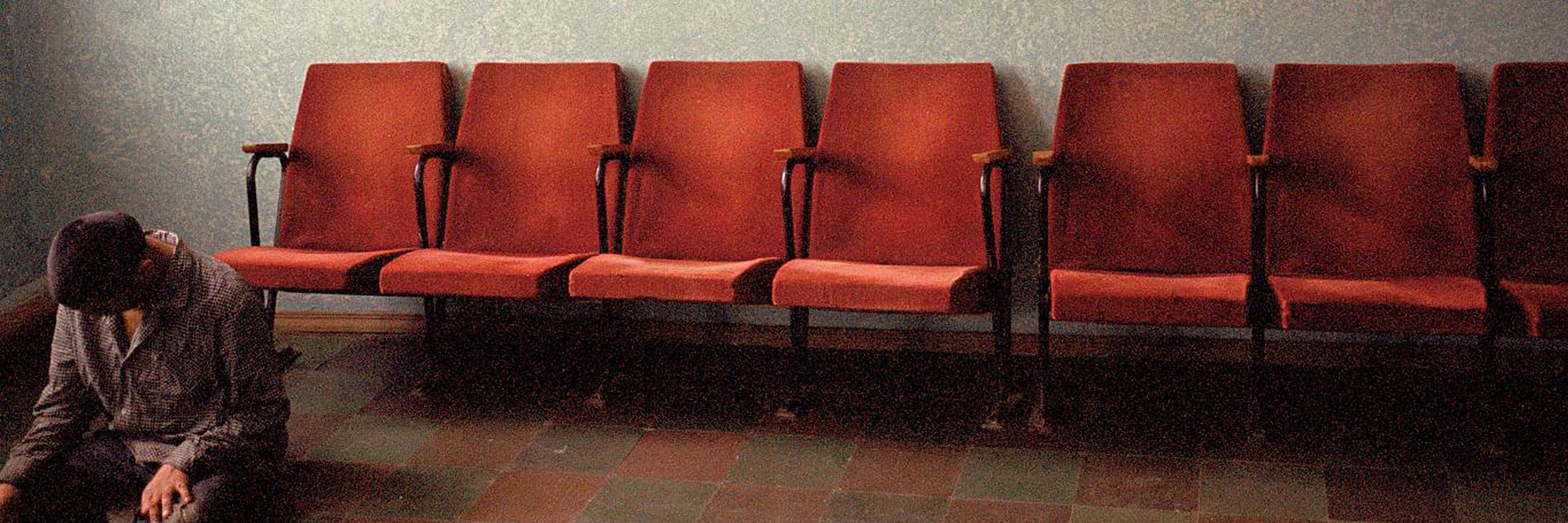 Person sitting on the floor, head down, empty chairs behind them