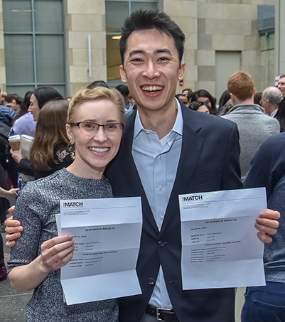 Laura Banashek (left) and Henry Su (right) holding up their Match Day letters, smiling