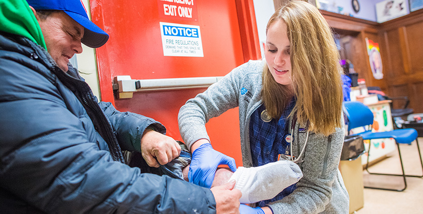 Image of female student examining foot of male homeless person