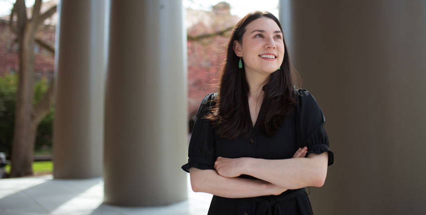 Alyssa Botelho, shot from the waist up in front of columns, looks off into the distance