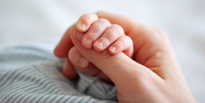A close up of an adult grasping the hand of an infant 